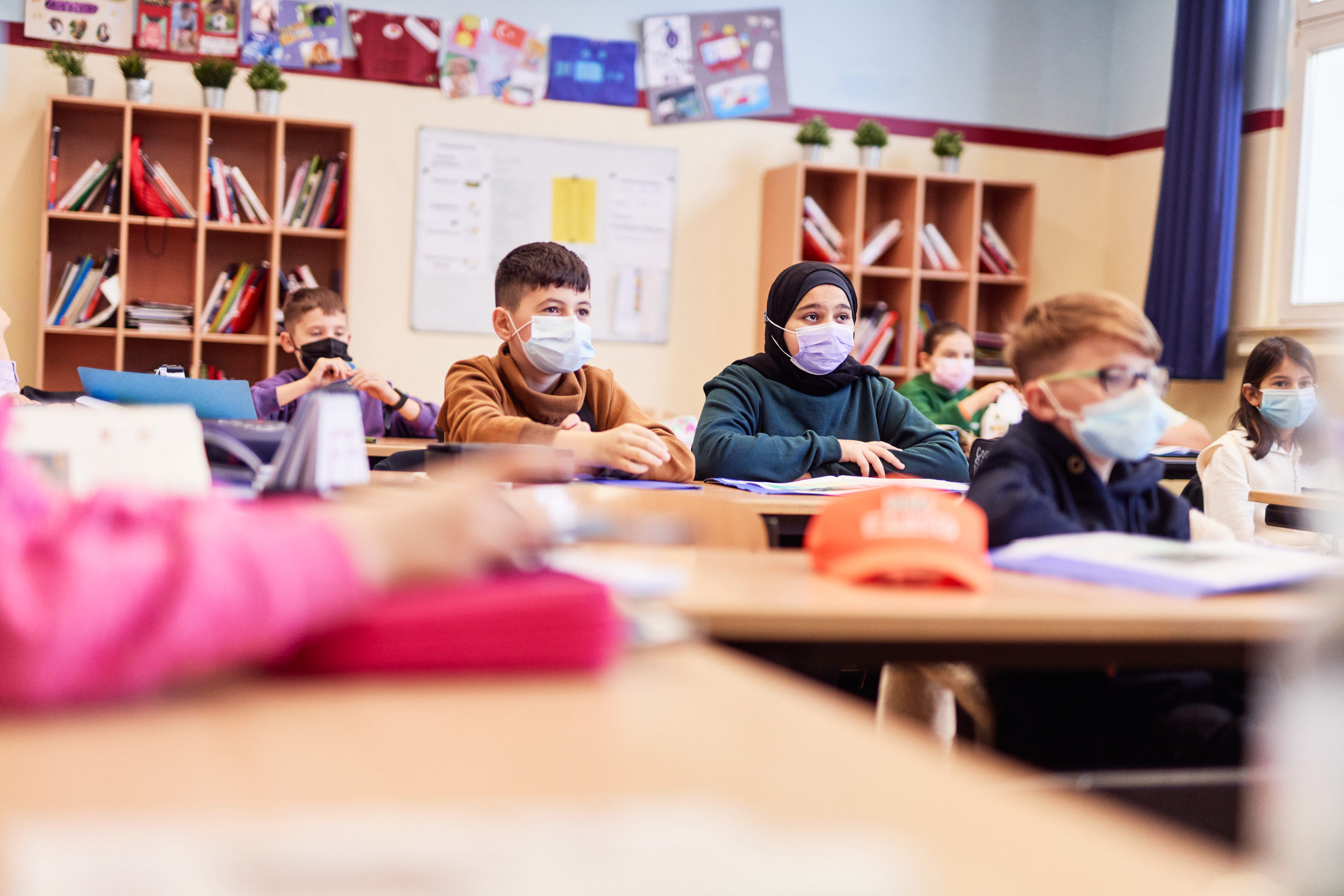 Schulkinder die Maske tragen und dem Unterricht zuhören.